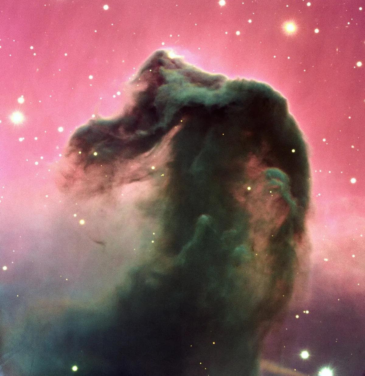 Image of the Horsehead Nebula showing a dark horse-head-shaped dust cloud silhouetted against a bright pink glowing background, with stars scattered around it.