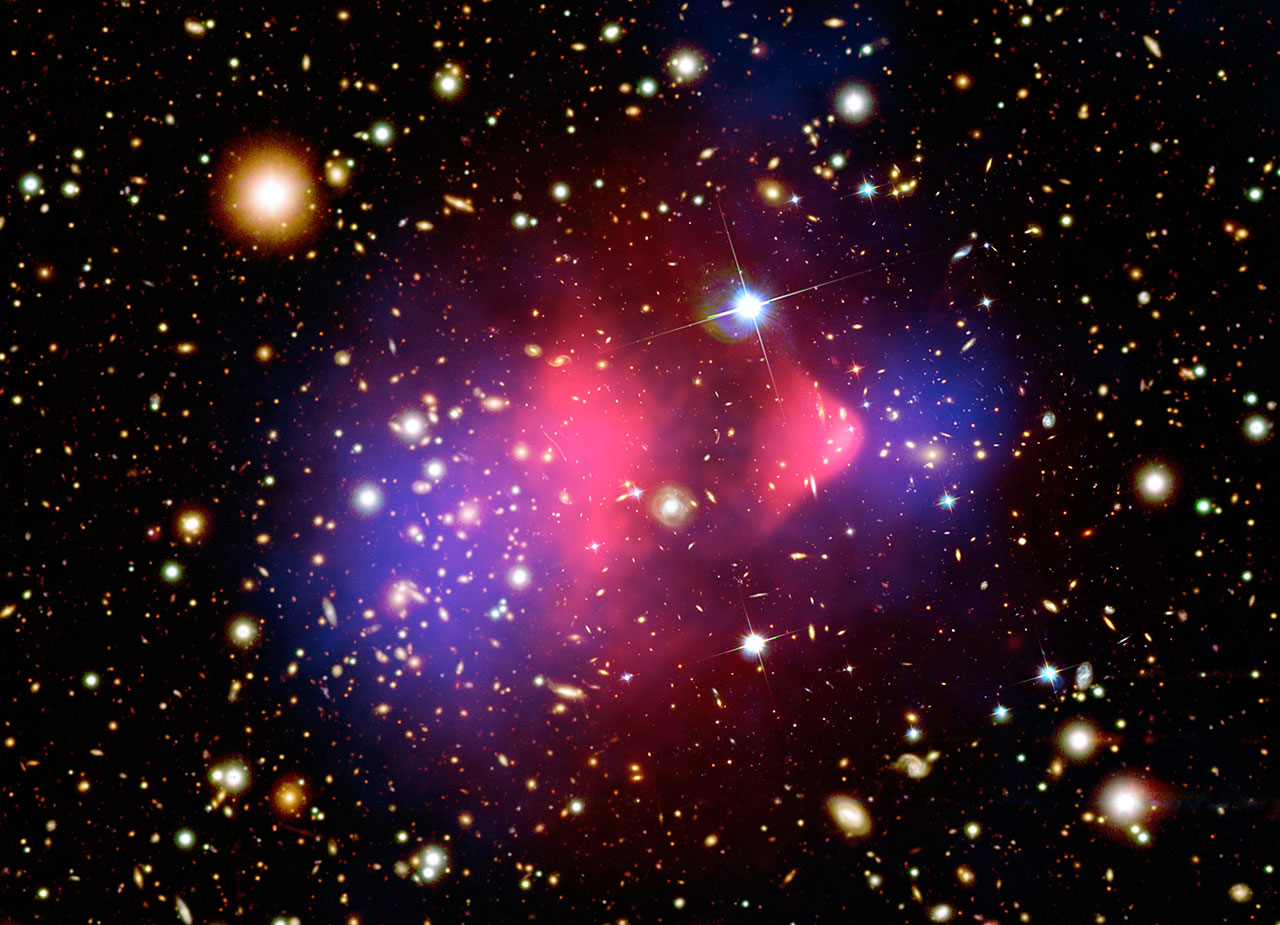 Composite image of the Bullet Cluster showing galaxies in visible light, pink X-ray emitting gas, and blue regions marking the gravitational-lensing mass distribution offset from the gas.