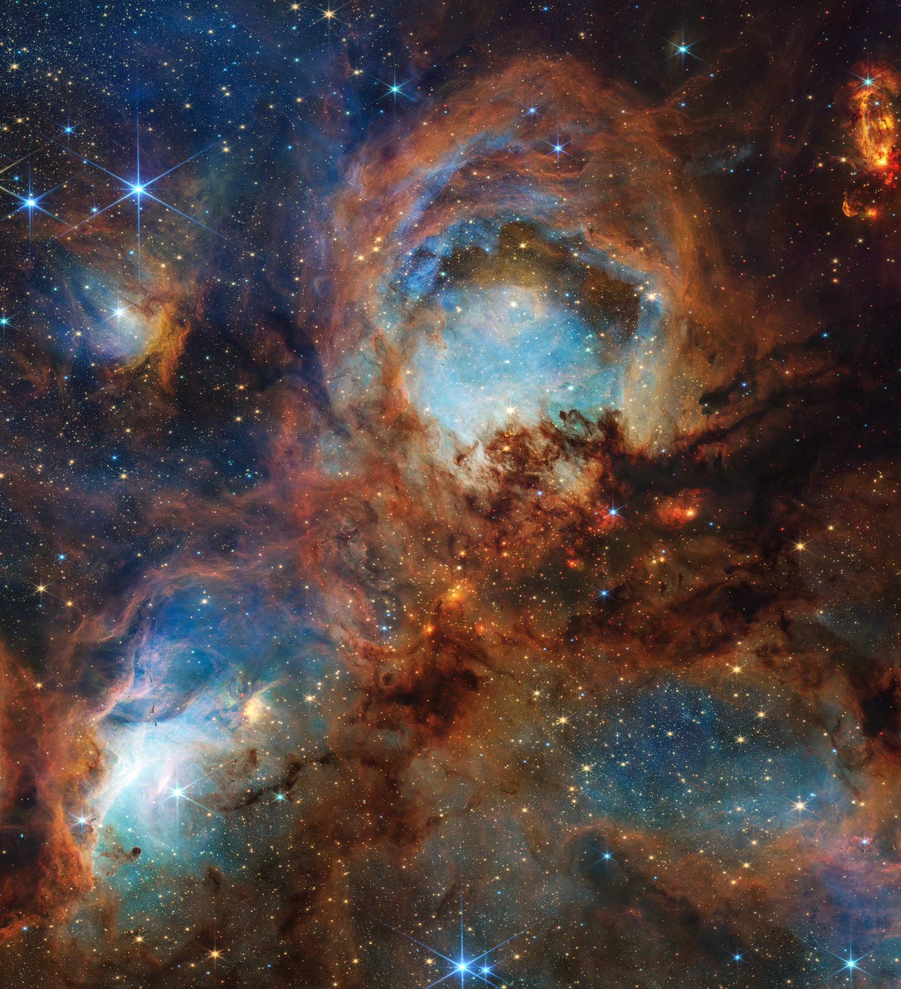 JWST infrared image of the Cat's Paw Nebula showing a bright blue-white cavity, orange and brown dust clouds, embedded young stars, and darker dusty lanes.
