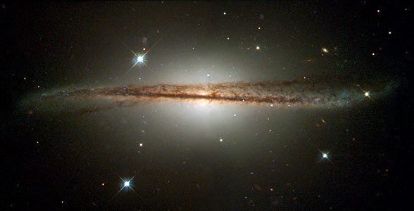 Edge-on spiral galaxy with a bright central bulge and a dark dust lane cutting across a thin disk whose outer regions appear warped or tilted.