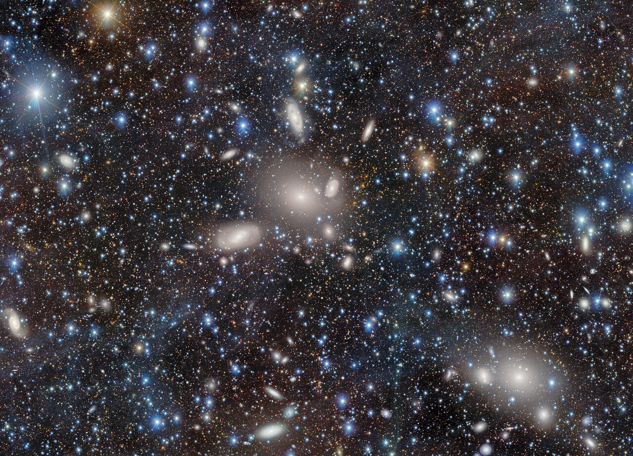 Wide-field image of the Antlia Cluster showing many stars and galaxies, including several large diffuse elliptical galaxies and numerous smaller galaxies across the field.