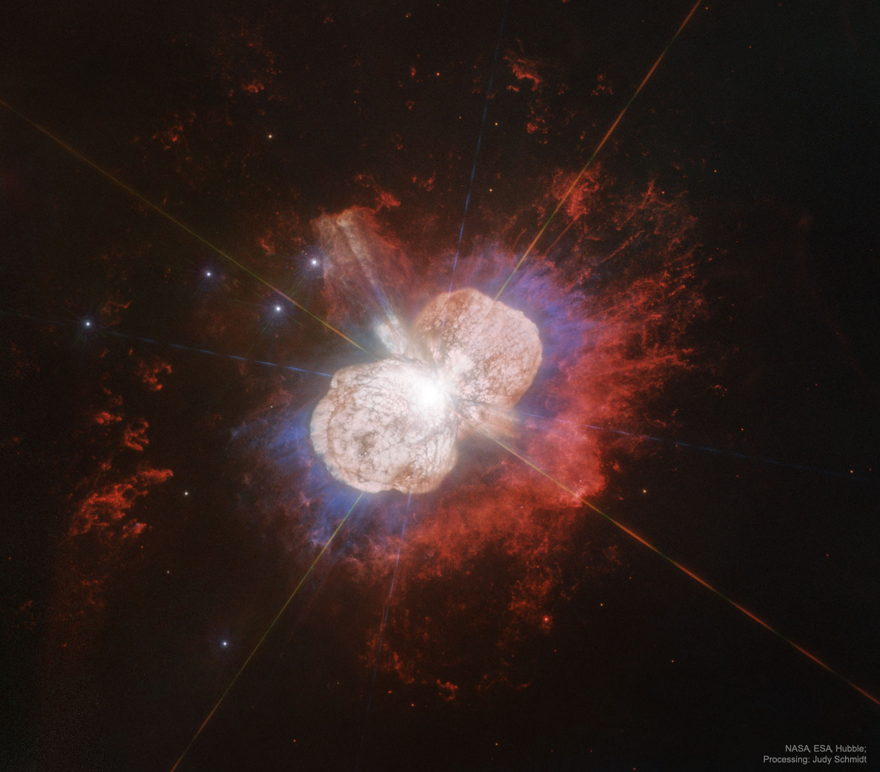 Hubble Space Telescope image of Eta Carinae showing a brilliant central star surrounded by two large bipolar lobes of ejected gas and dust (the Homunculus Nebula), glowing in orange-white with fainter red nebulosity extending outward.