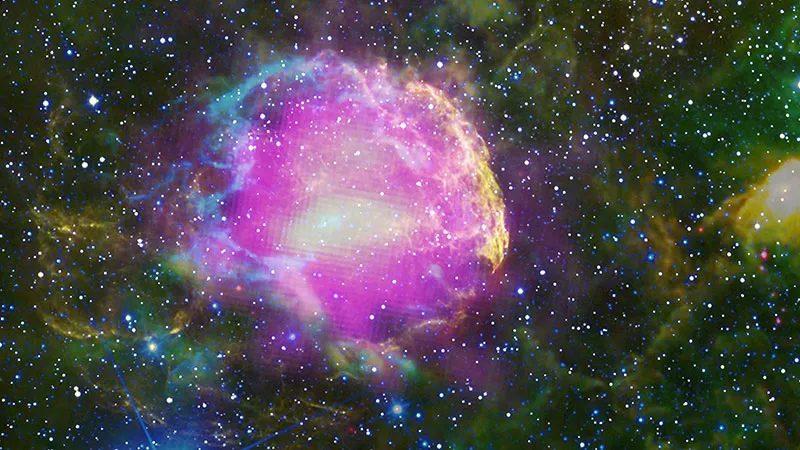 Gamma Rays Mark Cosmic Particle Accelerators: Supernova Remnant IC 443. Fermi gamma-ray emission (magenta) reveals where supernova shocks accelerate charged particles (electrons, protons, ions) to near light speed. When these cosmic rays collide with dense gas (cyan loops from WISE infrared), they produce gamma rays through pion decay — photons with energies >100 MeV that only arise from the universe’s most extreme particle acceleration. The infrared traces warm dust (blue to red: 3.4-22 \mu\mathrm{m}), while optical (yellow) shows heated gas. Only gamma rays directly probe the cosmic ray acceleration that makes SNRs nature’s particle accelerators. (Credit: NASA/DOE/Fermi LAT Collaboration, NOAO, and WISE)